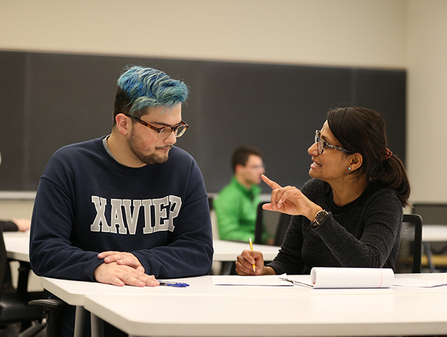 A Xavier student working with a professor at a desk in a classroom