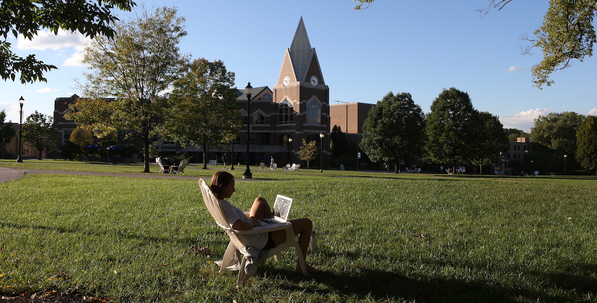 student sitting in front of Gallagher Student Center looking at laptop