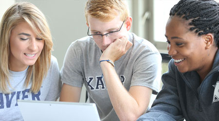 Three Xavier students smiling at a computer screen