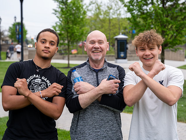 Two students posing with a mentor doing the X-Arms