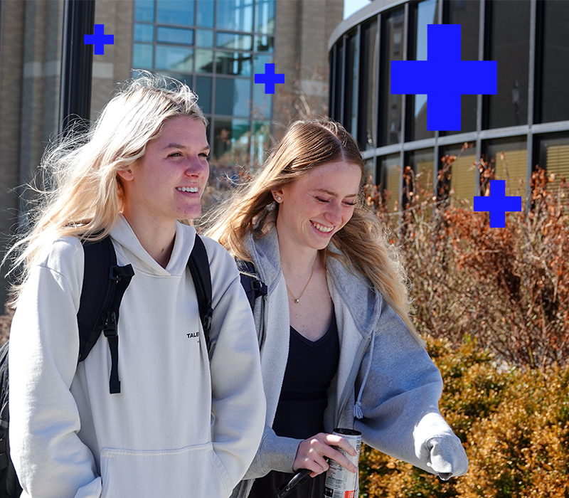 Four Xavier students walk down a paved sidewalk. They are surrounded by trees that are covered in red and orange leaves.