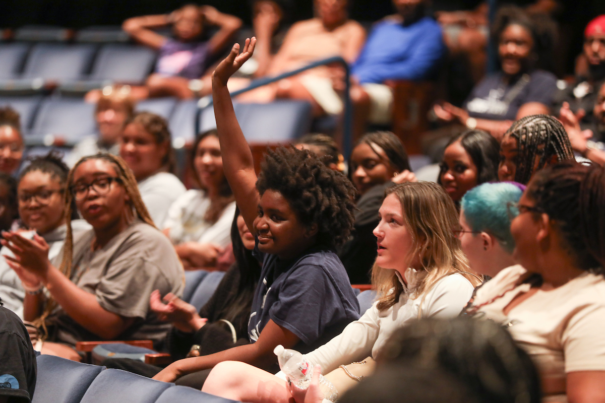 A photo of a student raising their hand in an audience.